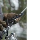 A gloved hand holds a fishing rod and a Dalstrong Fishing Hook Knife 5" from the Night Shark Series (NSF Certified), with blurred green foliage in the background.