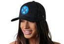 A woman with long brown hair smiles while wearing the Haka Hat Buffalo Trucker Hat, featuring a blue and red BUF X patch. The black snapback mesh cap by Haka Hat stands out against the white background.