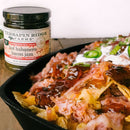 A black tray of loaded nachos topped with jalapeños, sour cream, and fiery Hot Habanero Bacon Jam, with a Terrapin Ridge Farms Hot Habanero Bacon Jam Quart jar in the background.