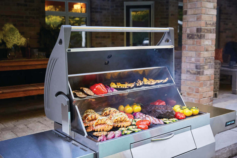 Napoleon PRO605CSS stainless steel charcoal cart grill with rear rotisserie burner and adjustable charcoal tray; view of food in grill and two shelves