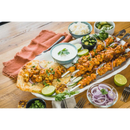 A platter of grilled chicken skewers cooked using the Napoleon Rotisserie Shish-Kebab Skewer Set (64008) by Napoleon Grills is served on naan bread with lime, red onions, cilantro, dipping sauce, cucumber slices, rice, and garnishes.