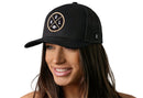 A smiling woman with long brown hair wears the Haka Hat New Orleans Trucker Hat—black mesh with “NOL X Football” design—standing out against a plain white background.