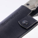 A close-up of the Messermeister Leather Belt Sheath for Overland Camp Knife shows the knife handle partly inside the black full-grain leather sheath, embossed with “Messermeister” and fastened by a metal snap button.