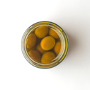 A top-down view of a glass jar filled with Taycte Antipasto Olive alla Monacale (MONACALE OLIVE) in brine, set against a white background, captures the essence of a traditional antipasto.