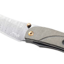 Close-up of the Messermeister Ojai Damasteel Folder - 3.75", an everyday carry knife featuring a patterned Damasteel blade, textured gray handle, and distinctive gold pivot screw and thumb stud.