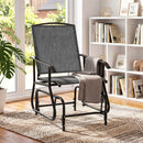The DirectDeals Outdoor Glider Chair with Metal Frame and Armrests, in modern gray, sits on a patterned rug near sunny windows, surrounded by plants, bookshelves, and decor with a blanket over one arm.