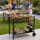 Four people enjoy food, drinks, and wine around the DirectDeals Outdoor Grill Cart with Stainless Steel Top and Storage at a backyard barbecue in a lush garden.