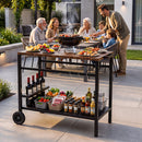 A family of six dines outdoors as the DirectDeals Outdoor Grill Cart with Stainless Steel Top and Storage holds meats, veggies, condiments, and wine on a modern patio surrounded by greenery.