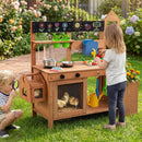 Two kids enjoy backyard fun with the Outdoor Wooden Mud Kitchen with Planter Box and Sink by DirectDeals. One cooks toy veggies, while the other checks chicks in a cage beneath the kitchen, surrounded by blooming flowers.