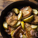 Pork chops cooked in a skillet with sliced green apples and shallots, seasoned with SALTOPIA Infused Sea Salts’ Saltopia French Mustard Salt: MUSTARD BEEN LOVE, served on a rustic wooden surface.