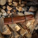 A Messermeister Overland Leather 5 Pocket Knife Roll With Pin Closure in cognac brown rests on a stack of chopped firewood.