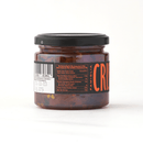 A glass jar with a black lid contains Taycte Famiglia Crispino Explosive Calabrian Hot Chili Peppers - Italian Peperoncini in Extra Virgin Olive Oil, featuring a nutrition label, barcode, and bold orange CRIS branding.