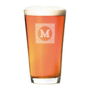 Pint Glasses - Set of 4: The Heirloom pint glass filled with amber beer, featuring an etched square emblem with the letter M in the center.