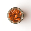 A glass jar of Famiglia Crispino Sun-Dried Tomato Antipasto — Italian Marinated in Olive Oil by Taycte, viewed from above on a white background—perfect for your next antipasto.