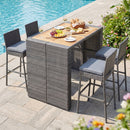 Four wicker barstools surround the DirectDeals Patio Acacia Wood Dining Set for Home, topped with wine, bread, fruit, and cheese by the pool—perfect for outdoor entertaining among flowers and greenery.