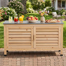 A wooden buffet table with drinks and snacks sits on a brick patio, paired with DirectDeals Outdoor Storage Cabinet with Stainless Steel Countertop and lawn chairs among blooming garden flowers.