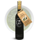 A bottle of Georgetown Olive Oil Co. Pesto Infused | High Polyphenols Extra Virgin Olive Oil with a tag is displayed in front of a bowl of green pesto sauce. This cold pressed extra virgin olive oil from Georgetown Olive Oil Co. delivers a rich, aromatic flavor that pairs perfectly with the vibrant pesto.
