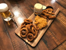 A wooden platter with onion rings, breaded chicken, mozzarella sticks, a side of Terrapin Ridge Farms Hoppin' Jalapeno Dip, assorted sauces, and a glass of beer on a rustic wooden table.