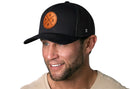A man wearing a Haka Hat Phoenix Trucker Hat Leather | Black PHX X Snapback and a beige shirt is smiling, facing slightly right, on a plain white background.