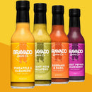 Four Bravado Spice Co. hot sauce bottles are arranged in a row against a yellow background: Bravado Spice Co Pineapple & Habanero Hot Sauce, Creamy Herb & Jalapeno, Serrano & Basil, and Ghost Pepper & Blueberry. Each fruit-forward hot sauce from Bravado Spice Co adds its own bold flavor—whether you want the vibrant kick of a tropical sauce or the balanced sweet heat of Pineapple & Habanero.