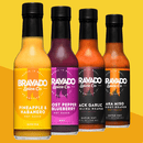 Four bottles of Bravado Spice hot sauce are displayed side by side, showcasing the following flavors: Pineapple & Habanero, Ghost Pepper Blueberry, Black Garlic Carolina Reaper, and Aka Miso Ghost-Reaper. The Bravado Spice Pineapple & Habanero Hot Sauce stands out as a vibrant and tropical option—perfect for adding a zesty kick to your favorite summer seafood glaze.