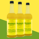Three bottles of Bravado Spice Pineapple & Jalapeño Margarita Mixer, a vibrant mixer from Bravado Spice featuring bright yellow labels and black caps, are displayed against a green and yellow background.