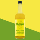 A bottle of Bravado Spice Co Pineapple & Jalapeño Margarita Mixer—a premium craft cocktail mixer from Bravado Spice Co—is displayed against a yellow and green diagonal background. The label features a vibrant yellow design with green and white text, showcasing this bold Pineapple & Jalapeño Margarita Mixer, ideal for elevating your next cocktail experience.
