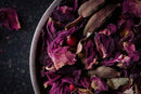 A close-up of a bowl filled with dried rose petals, red berries, and whole cardamom pods from World Spice Pink Chai by World Spice, creating a colorful and textured arrangement reminiscent of the fragrant ingredients found in an herbal chai latte.