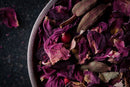 A close-up of a bowl filled with dried rose petals, whole green cardamom pods, and a few small red berries on a dark background—perfect inspiration for crafting your own elegant herbal blend or enjoying as part of the World Spice Loose-Leaf Tea Tasting Flight by World Spice.