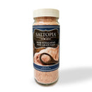 A clear jar of SALTOPIA Infused Sea Salts Himalayan pink fine grain 16oz features visible pink salt and a label with an image of salt and a wooden spoon, showcasing its rich essential minerals.