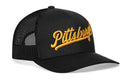 The Haka Hat Pittsburgh Gold Script Trucker Hat is a black mesh snapback featuring bold gold "Pittsburgh" embroidery across the front from Haka Hat.