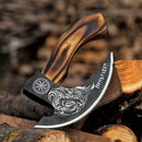 The Texan Knives Custom Hand-Engraved Pizza Axe features an 8-inch J2 steel blade with detailed engravings and a curved wooden handle, displayed on split logs against a blurred woodpile background.