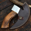 A Texan Knives Forged Pizza Cutter with a custom handmade J2 steel blade and wood handle rests on a wooden surface. The blade is partly covered by a curved, brown leather sheath featuring white stitching and a buttoned strap.