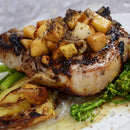 A grilled chop seasoned with SALTOPIA Bacon Maple Seasoning: JURASSIC PORK sits atop roasted potatoes and broccolini, finished with diced apples and a sweet-smoky sauce, all from SALTOPIA Infused Sea Salts.