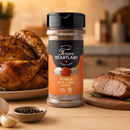 A bottle of Texan Heartland Pork & Poultry Seasoning by Texan Heartland rests on a table alongside roasted chicken, sliced pork, garlic, black peppercorns, and fresh herbs in a cozy kitchen. Its savory aroma fills the air, making it the ideal choice for grilling chicken or enhancing your favorite meals.