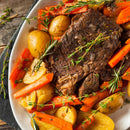 A plate of pot roast with tender beef, chunked baby potatoes and carrots, garnished with rosemary and thyme. The dish is well-cooked and seasoned with SALTOPIA Infused Sea Salts’ Garlic Salt: MOUTH FULL OF MAGIC for extra flavor.