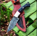 The Texan Knives Premium Damascus Steel Hunting Knife, featuring a resin and buffalo horn handle, rests on its leather case atop a green wooden bench outdoors.