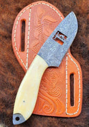 The Texan Knives Cowboy Bull Cutter Knife features a custom handmade Damascus steel blade and a smooth camel bone handle, resting on an embossed, stitched leather sheath atop brown fur—exemplifying authentic Western craftsmanship.