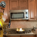 A firefighter in uniform uses the Prepared Hero Fire Spray by Prepared Hero to extinguish a flaming pan on a stovetop, demonstrating proper kitchen fire safety techniques.