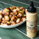 A bottle of Terrapin Ridge Farms Creamy Garlic Mustard Squeeze is in the foreground, with a plate of pretzel bites drizzled with the mustard blurred in the background, all set on a green tablecloth.