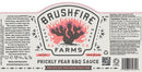 The Brushfire Farms Prickly Pear BBQ Sauce label displays a stylized pink and black cactus, detailed product information, ingredient list, and social media handles. The text emphasizes its Texas heritage and the use of genuine prickly pear to deliver an authentic savory BBQ sauce experience.