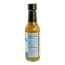 A clear glass bottle with a black cap holds a yellowish sauce. The back label provides nutrition facts and ingredients for this all-natural Powerful Pepper Serrano Pineapple Plantain Hot Sauce from the Powerful Pepper Company. Upright on a white background, the bottle highlights the vibrant appeal of this unique hot sauce.