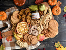 A wooden board with pumpkin bread, cookies, pizzelles, mini donuts, pretzels, apples, pears, a bowl of swirled pumpkin dip, and Terrapin Ridge Farms Pumpkin Butter—perfect for entertaining amid pumpkins and fall leaves.