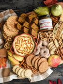 A fall-themed charcuterie board for entertaining, with pumpkin bread, cookies, pretzels, apple slices, biscotti, pizzelle, powdered donuts, caramel dip, pears, and Terrapin Ridge Farms Pumpkin Butter by Terrapin Ridge Farms on a checkered cloth.