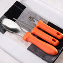 Three orange-handled utensils—a spoon, serrated knife, and fork—from the Messermeister Pumpkin Carving Set (3 Piece) rest on a folded black-and-white checkered napkin atop a white rectangular plate.