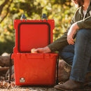 Red 25-quart cooler by Bison Coolers, with a man in a green shirt and jeans reaching inside.