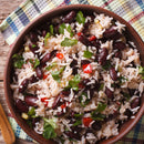A bowl of rice with red kidney beans, chopped red peppers, and fresh parsley sits on a colorful checked cloth atop a rustic wooden table, perfectly seasoned with SALTOPIA Infused Sea Salts’ Garlic & Onion Salt: ROOT MATES for extra flavor.