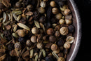 A close-up of a metal bowl filled with various whole spices—such as coriander seeds, black peppercorns, cloves, and fennel seeds—showcasing their vibrant textures and colors: the perfect ingredients for creating an authentic World Spice Roast Chai blend by World Spice, crafted from freshly roasted spices for a robust chai experience.