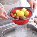 A person uses the Lovely Home Icon Silicone vegetable and fruit cleaning and drainage basket— a folding water filter net—to rinse assorted fruits including strawberries, lemon, apple, and kiwi under running water in the kitchen sink.