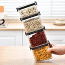 A hand holds four stacked Lovely Home Icon 1-4PCS Sealed Jars Kitchen Organizer Grain Storage Boxes, each filled with white beans, mixed beans, dried red berries, and spiral pasta in a kitchen setting.